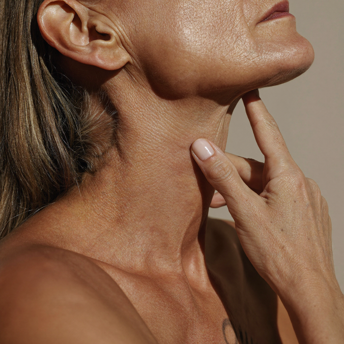 Profile of a woman in her fifties, fingertips along her jawline and neck