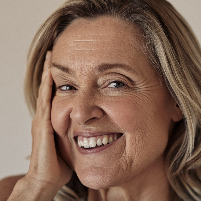 Woman in her late fifties smiling, hand resting at her temple
