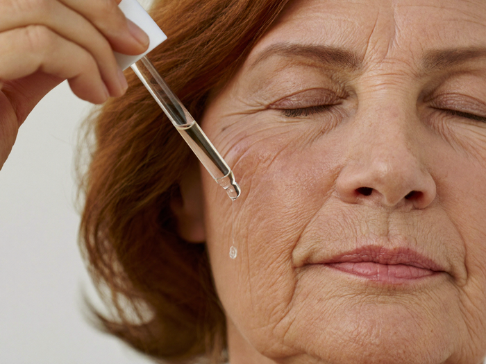 Woman in her fifties holding a serum dropper above her cheekbone